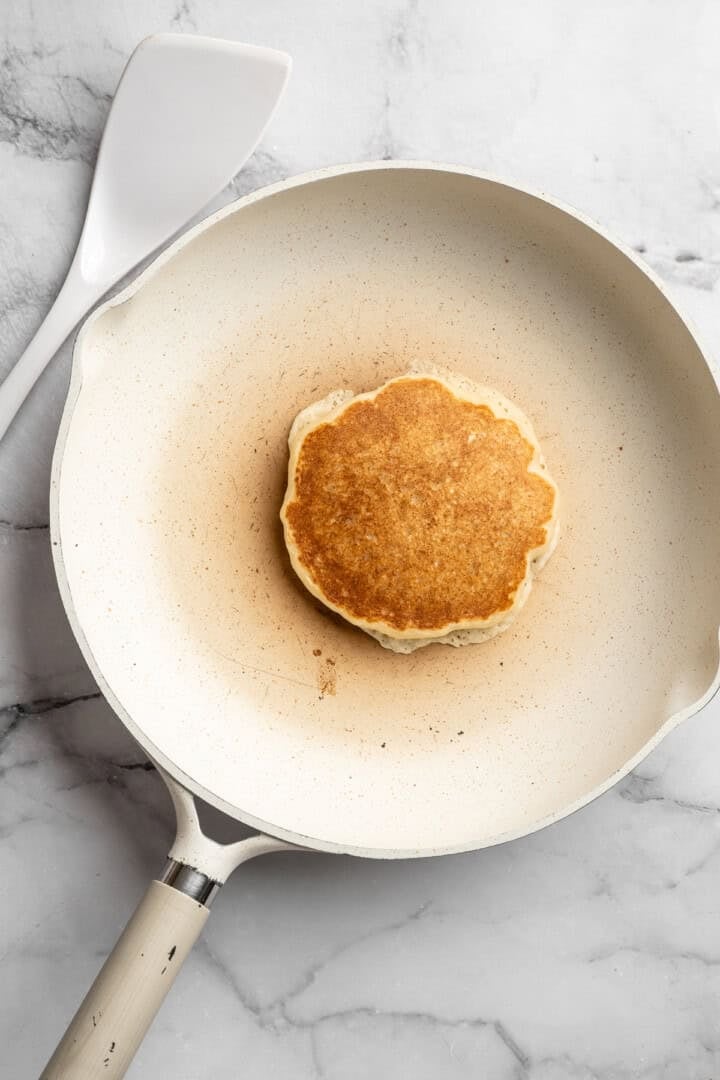Easy to make and SO light and fluffy, these vegan cottage cheese pancakes are about to become your go-to, protein-packed breakfast. Cooking a vegan cottage cheese pancake in a skillet (after flipping).