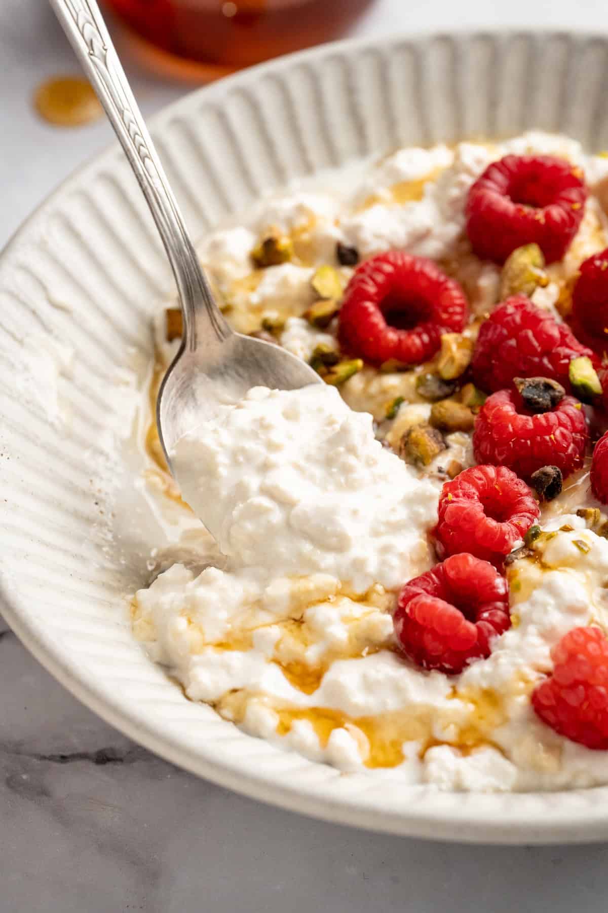 This vegan cottage cheese recipe marinates perfectly tender tofu "curds" in a savoury, tangy, salty sauce. It's a vegan staple you need! A spoon dipping into a bowl with vegan cottage cheese and berries.