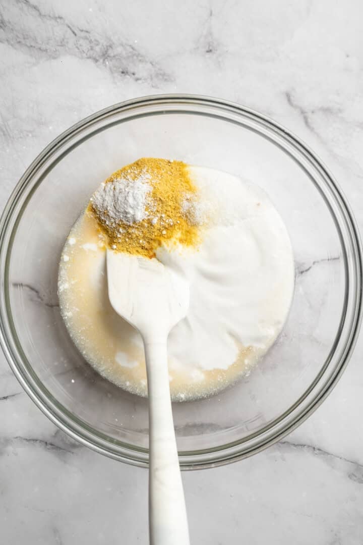 This vegan cottage cheese recipe marinates perfectly tender tofu "curds" in a savoury, tangy, salty sauce. It's a vegan staple you need! Adding vegan Greek yogurt, nutritional yeast, lemon juice, lactic acid powder, and sea salt to a bowl.