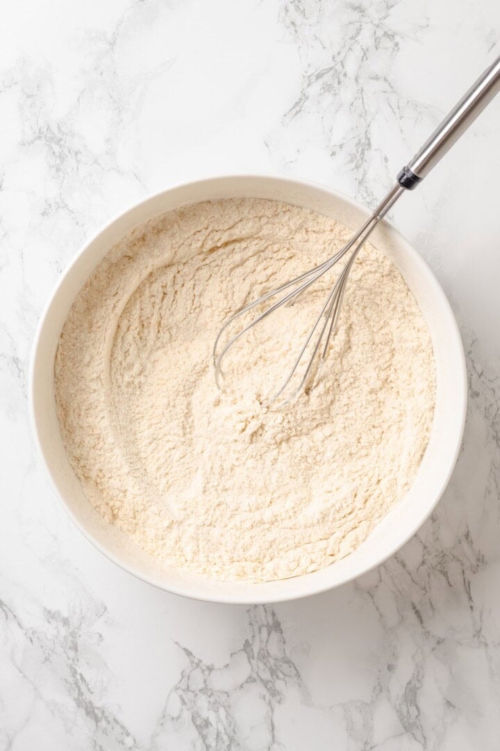 This vegan yellow cake is made of two layers of moist, tender, golden-yellow cake, filled and frosted with silky chocolate buttercream. Whisking together flour, baking soda, salt, and turmeric for vegan yellow cake.