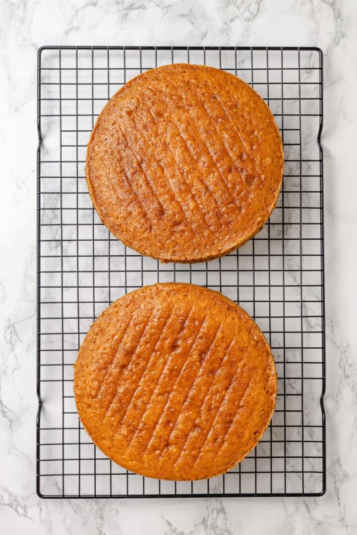 This vegan yellow cake is made of two layers of moist, tender, golden-yellow cake, filled and frosted with silky chocolate buttercream. Two layers of vegan yellow cake cooling on a wire wrack.