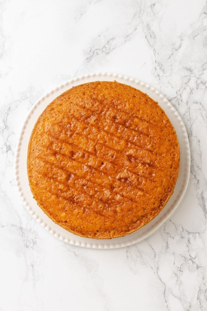 This vegan yellow cake is made of two layers of moist, tender, golden-yellow cake, filled and frosted with silky chocolate buttercream. One layer of vegan yellow cake on plate.