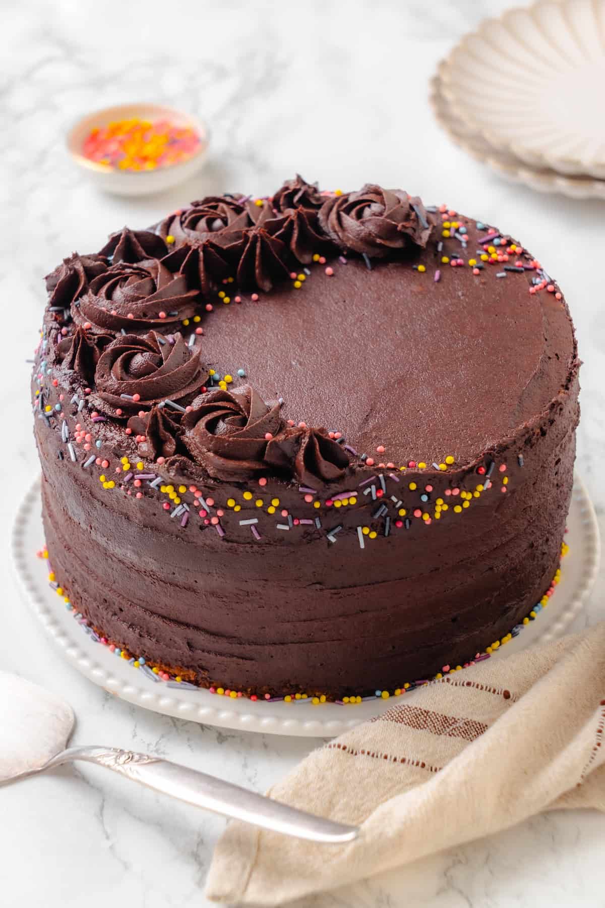 This vegan yellow cake is made of two layers of moist, tender, golden-yellow cake, filled and frosted with silky chocolate buttercream. Vegan yellow cake with chocolate frosting and rainbow sprinkles.