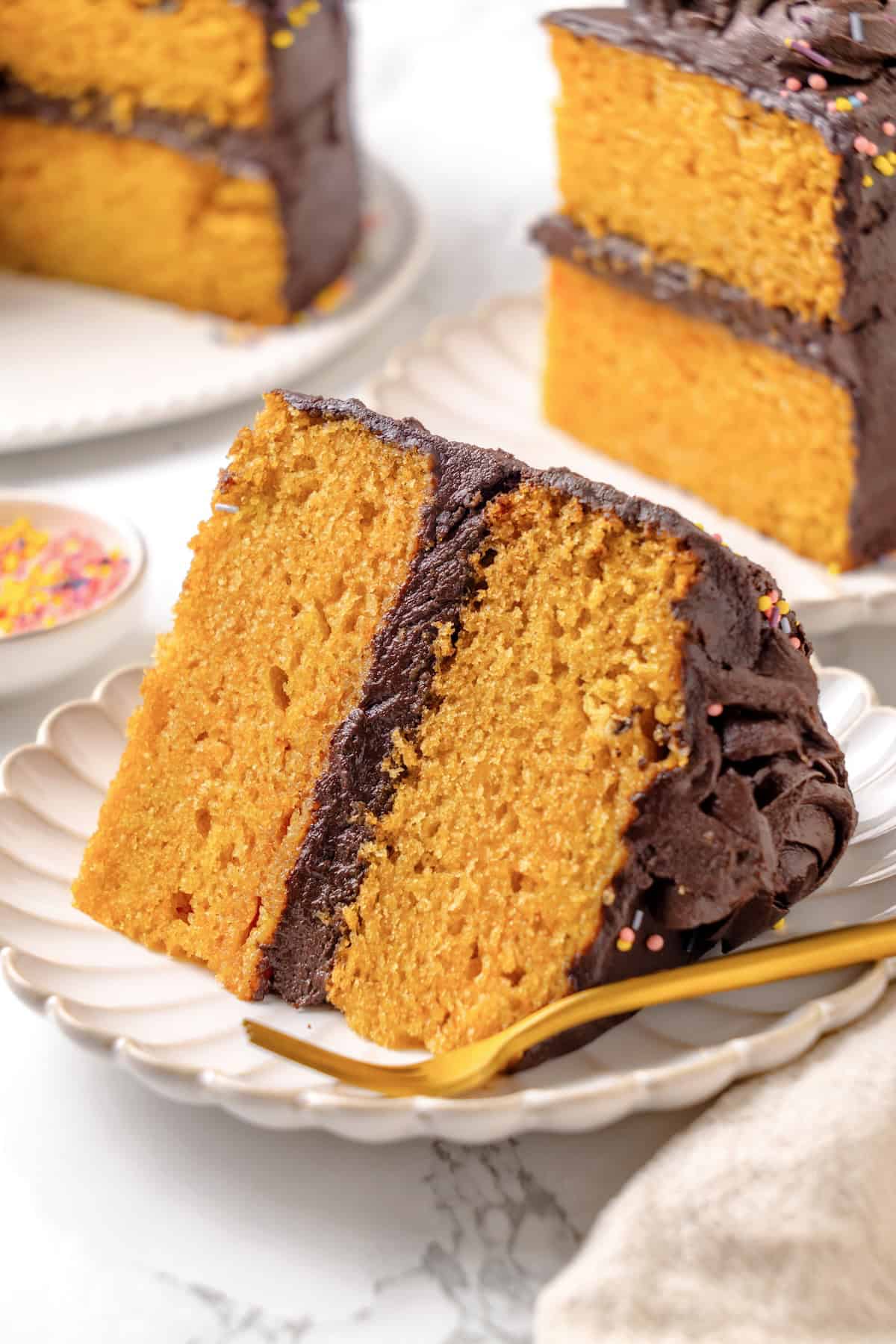 This vegan yellow cake is made of two layers of moist, tender, golden-yellow cake, filled and frosted with silky chocolate buttercream. A slice of vegan yellow cake on a plate.