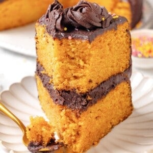 A slice of vegan yellow cake upright on a plate with a bite taken out of it.
