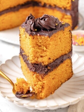 A slice of vegan yellow cake upright on a plate with a bite taken out of it.