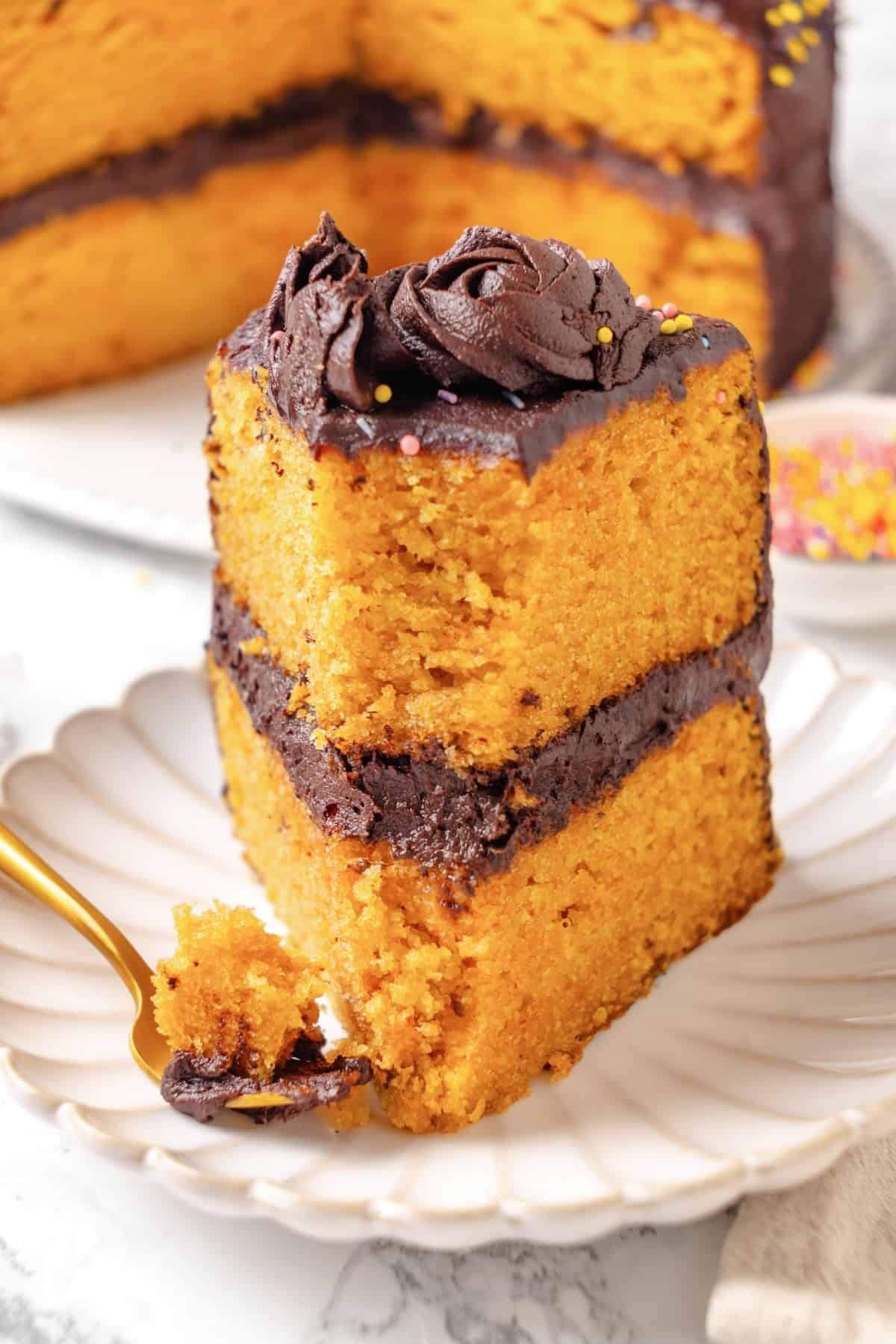 This vegan yellow cake is made of two layers of moist, tender, golden-yellow cake, filled and frosted with silky chocolate buttercream. A slice of vegan yellow cake upright on a plate with a bite taken out of it.
