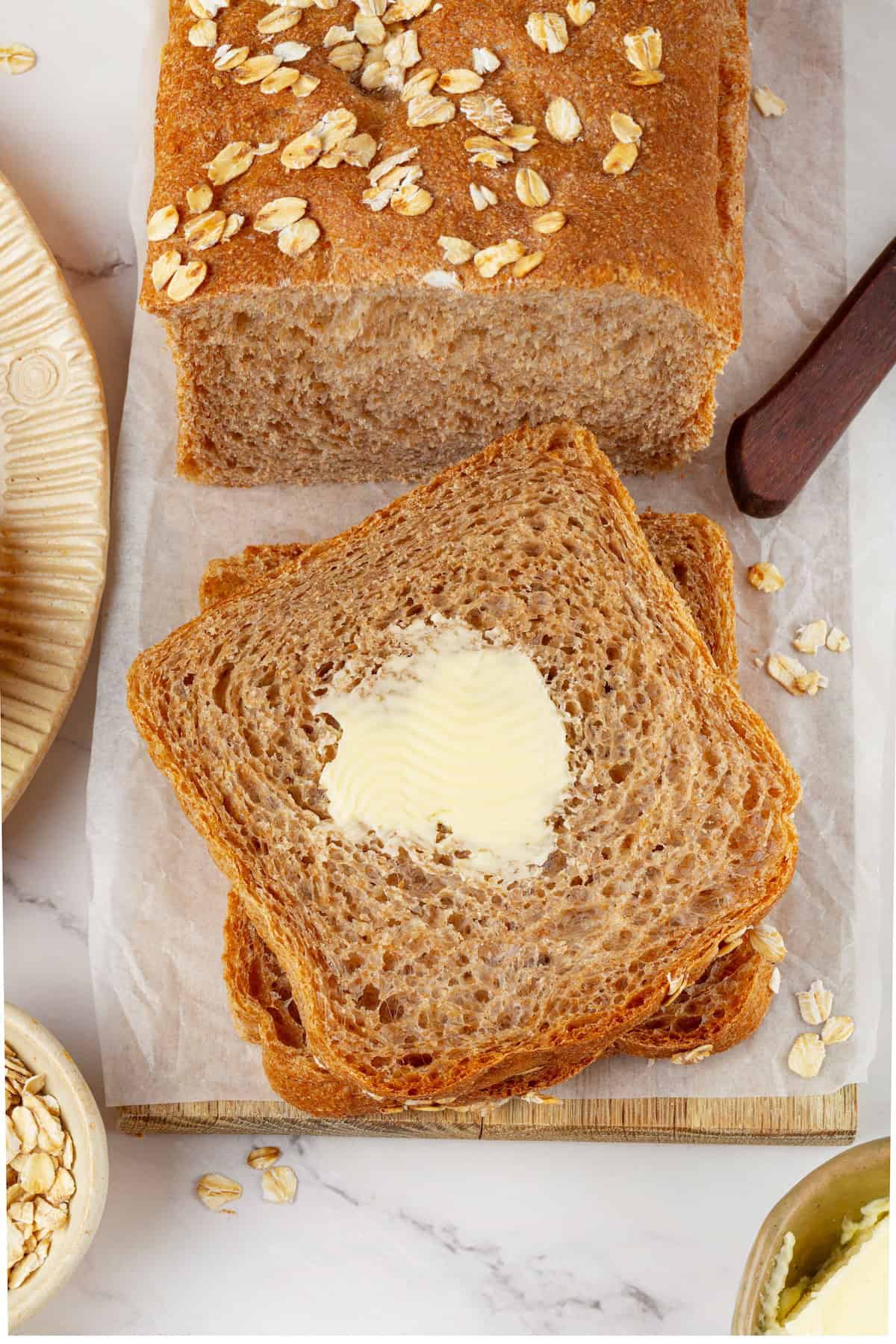 Looking for the perfect slice to build your PB&J or avocado toast on? This soft, tender whole grain sandwich bread is for you. Overhead image of a loaf of whole grain sandwich bread with buttered slices cut from it.