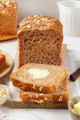 A loaf of whole grain sandwich bread with buttered slices cut from it.