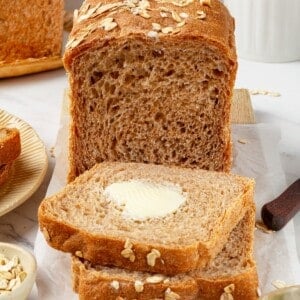 A loaf of whole grain sandwich bread with buttered slices cut from it.