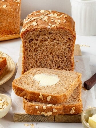 A loaf of whole grain sandwich bread with buttered slices cut from it.