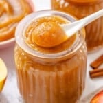 A spoon holding a scoop of apple butter above a jar.