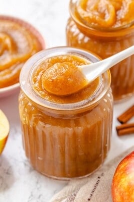 A spoon holding a scoop of apple butter above a jar.