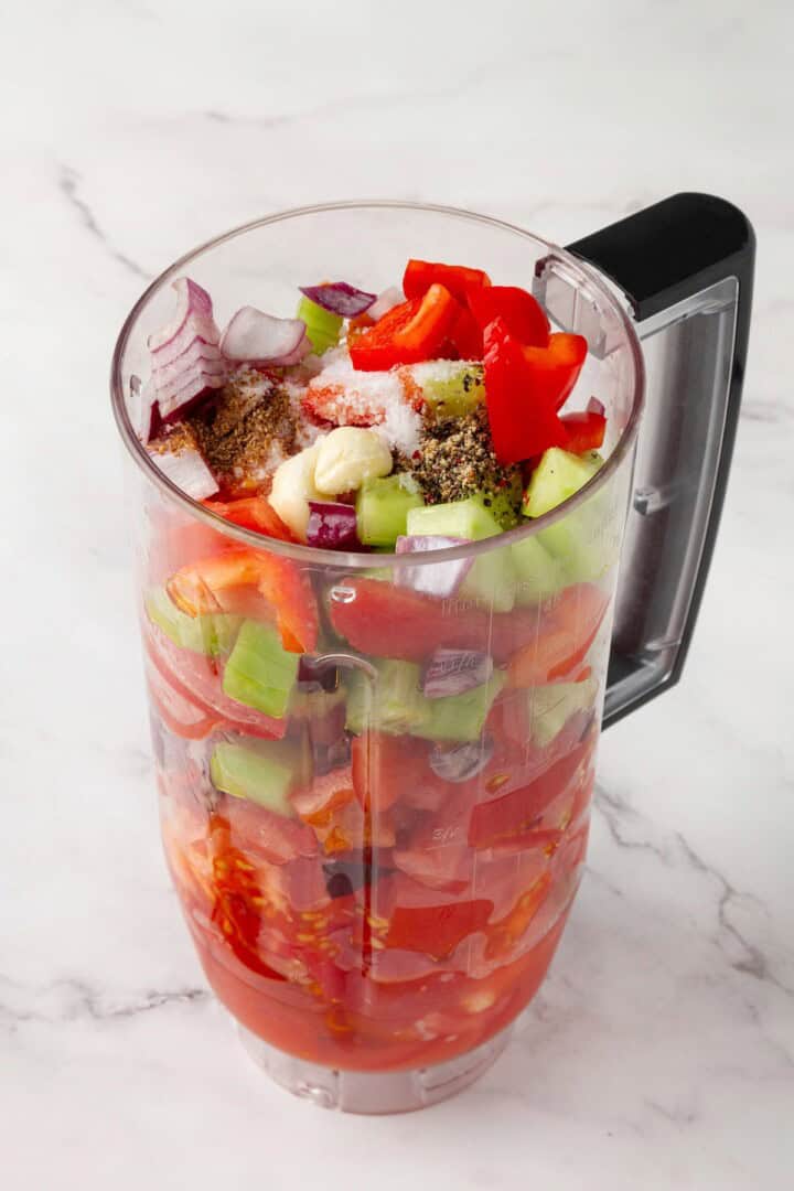 This gazpacho recipe blends farmers' market tomatoes with fresh veggies, olive oil, and vinegar for the perfect sweet 'n tangy summer soup. A blender loaded with tomatoes, cucumber, red bell pepper, red onion, garlic, olive oil, red wine vinegar, and seasonings.