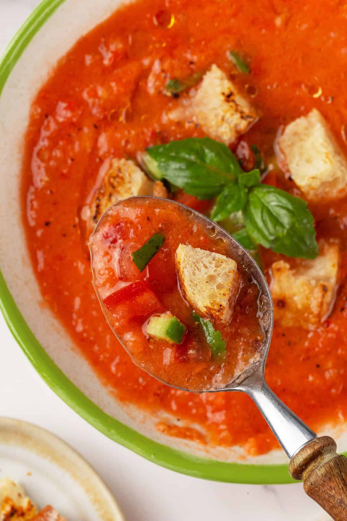 This gazpacho recipe blends farmers' market tomatoes with fresh veggies, olive oil, and vinegar for the perfect sweet 'n tangy summer soup. A spoon holding a scoop of gazpacho up to the camera.