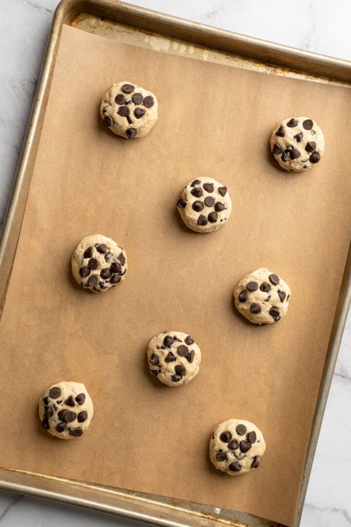 These vegan sourdough chocolate chip cookies are about to up your cookie standards. They're tender and chewy with a subtle sourdough tang. Sourdough chocolate chip cookie dough formed into balls and arranged on a baking sheet.