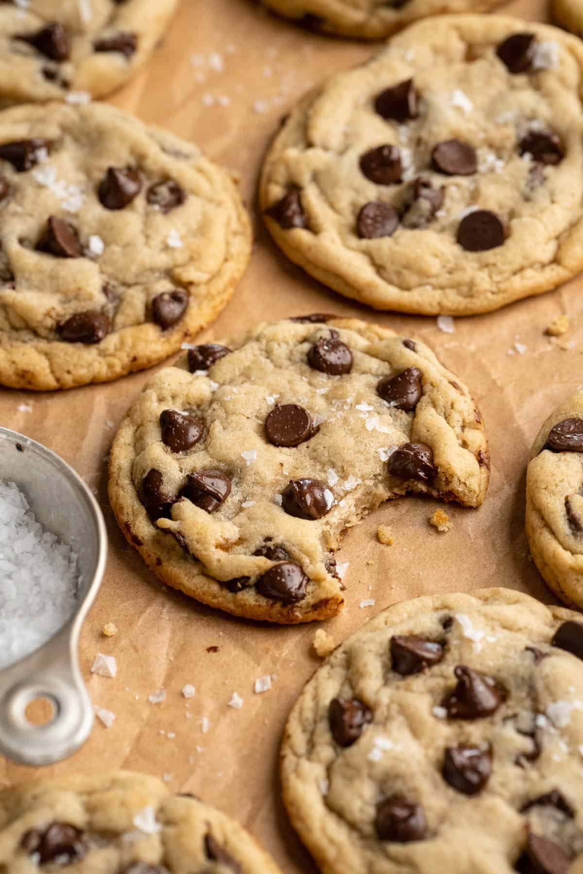 These vegan sourdough chocolate chip cookies are about to up your cookie standards. They're tender and chewy with a subtle sourdough tang. Sourdough chocolate chip cookies spread out on parchment paper. One has a bite taken out of it.
