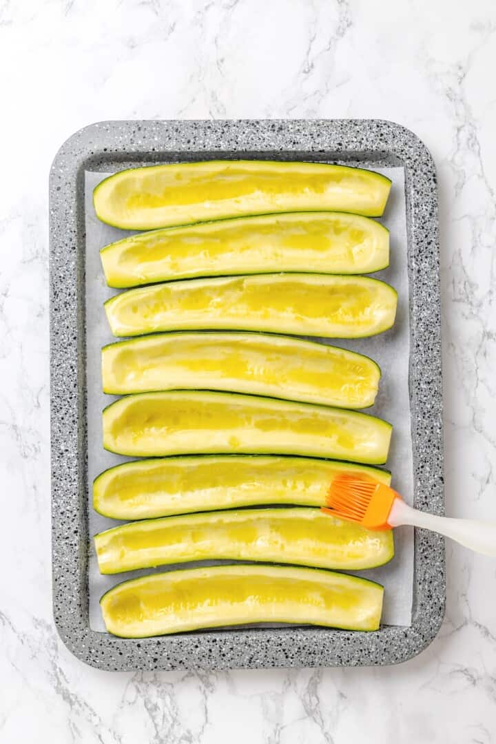 These stuffed zucchini boats are loaded with rich marinara sauce, melty vegan mozzarella, and protein-packed lentils. The perfect summer side. Brushing zucchini boats with olive oil.