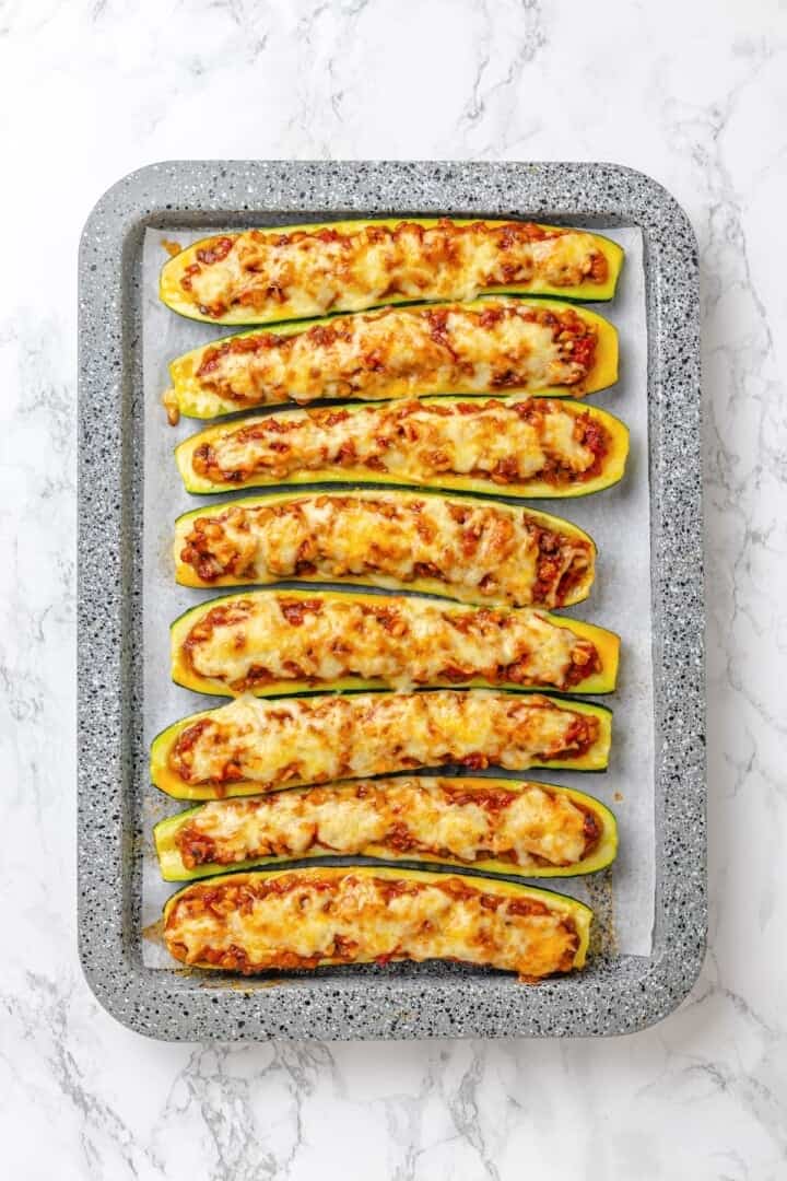 These stuffed zucchini boats are loaded with rich marinara sauce, melty vegan mozzarella, and protein-packed lentils. The perfect summer side. Overhead image of stuffed zucchini boats on a sheet pan.