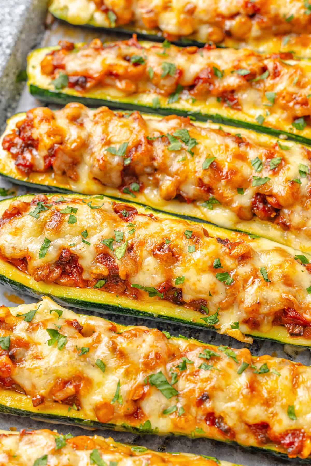 These stuffed zucchini boats are loaded with rich marinara sauce, melty vegan mozzarella, and protein-packed lentils. The perfect summer side. Closeup of lentil-stuffed zucchini boats on a sheet pan.