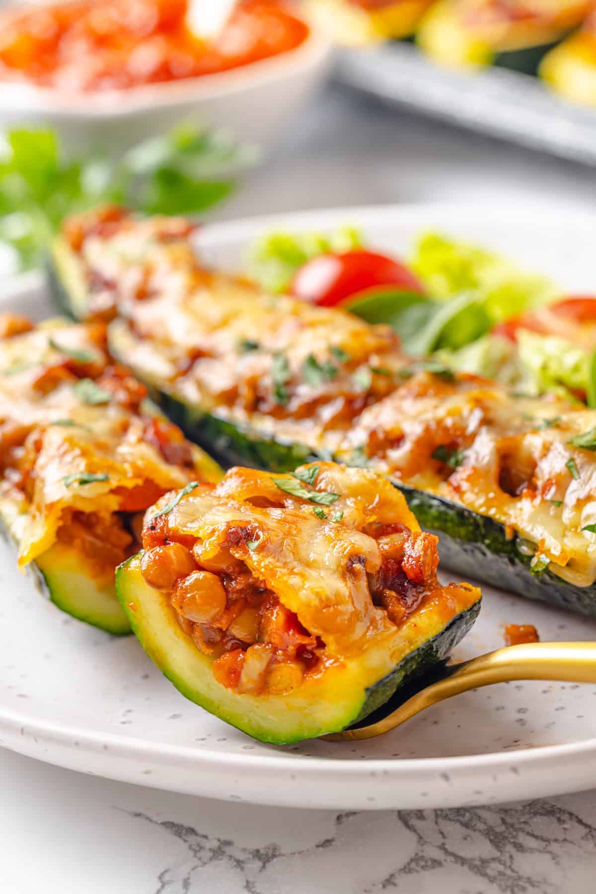 These stuffed zucchini boats are loaded with rich marinara sauce, melty vegan mozzarella, and protein-packed lentils. The perfect summer side. A fork holding a bite of stuffed zucchini.