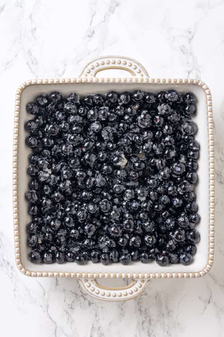 Blueberries tossed with lemon zest, sugar, melted vegan butter, and vanilla in a baking dish.