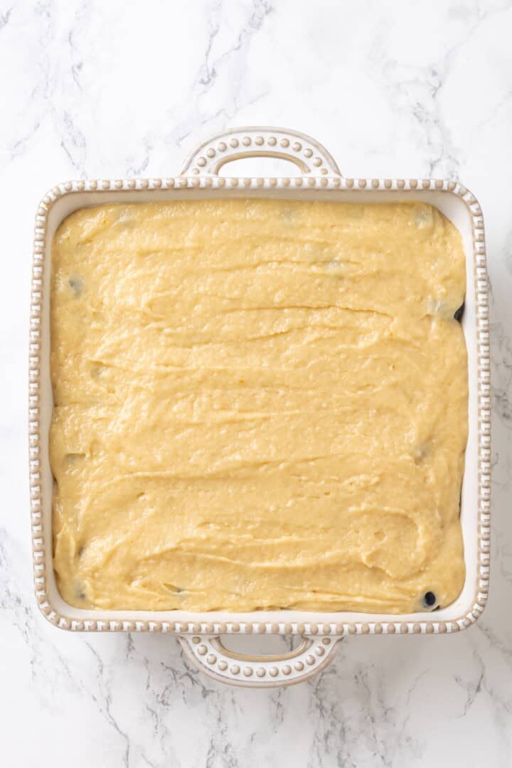 Cobbler batter spread over blueberry filling in a baking dish.