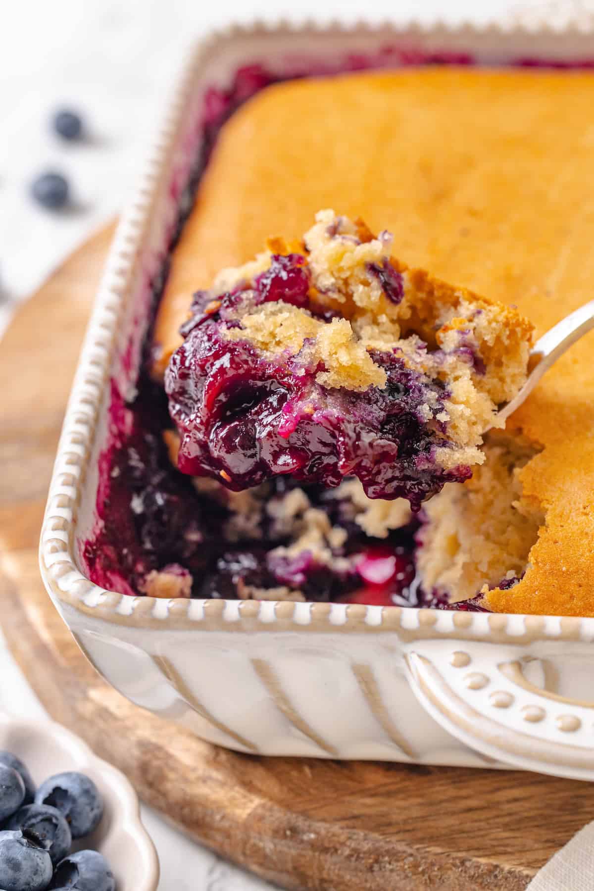 A serving spoon holding a scoop of vegan blueberry cobbler over the baking dish.