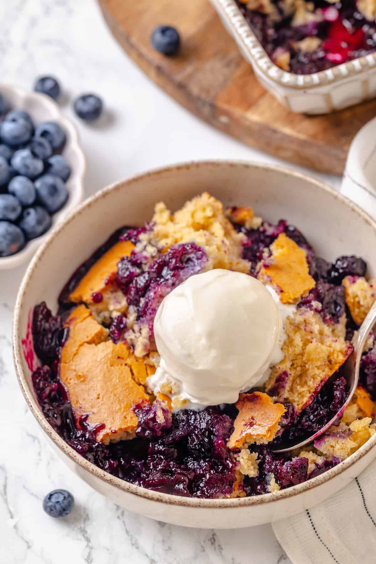 A bowl of blueberry cobbler topped with vegan vanilla ice cream.