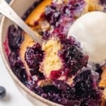 A spoon scooping into a serving of blueberry cobbler with vanilla ice cream.