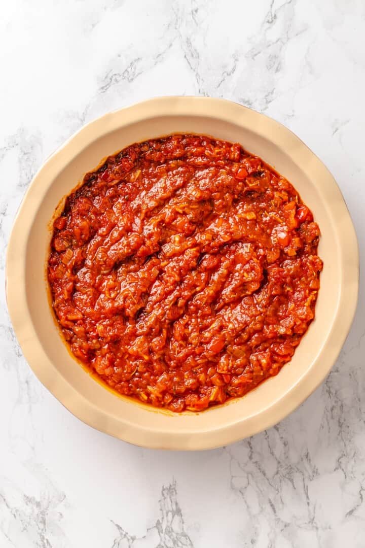This easy ratatouille recipe boasts colourful layers of eggplant, squash, and tomato in a rich, tangy tomato sauce with delicate herb oil. Adding tomato sauce to the bottom of a round baking pan.