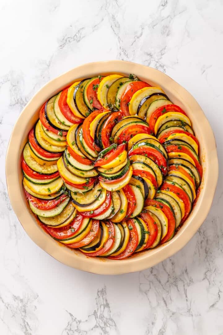 This easy ratatouille recipe boasts colourful layers of eggplant, squash, and tomato in a rich, tangy tomato sauce with delicate herb oil. Classic french ratatouille ready to go in the oven.