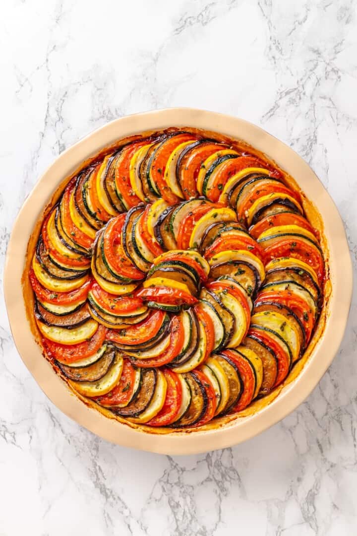 This easy ratatouille recipe boasts colourful layers of eggplant, squash, and tomato in a rich, tangy tomato sauce with delicate herb oil. Classic french ratatouille cooling in the baking dish.