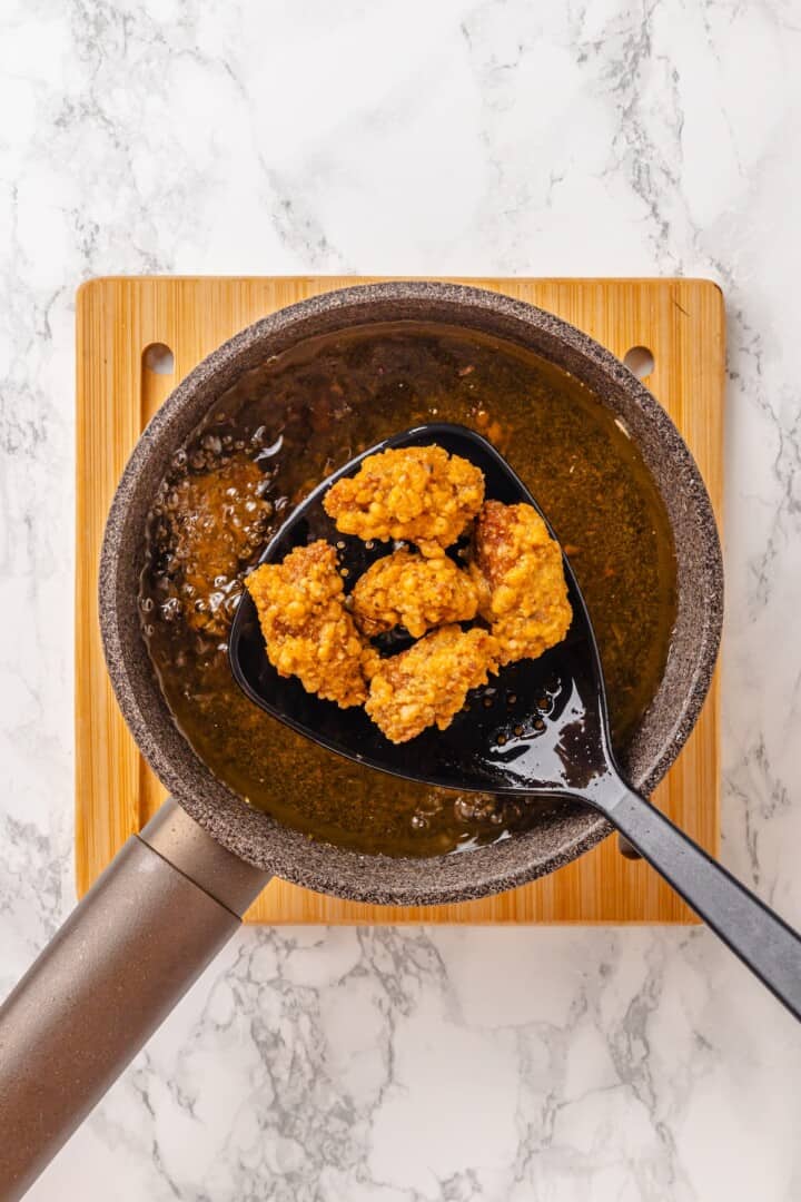 Vegan popcorn chicken features tender soy curls in a crunchy KFC-style breading served with a maple Dijon sauce. It beats takeout any day! Removing fried vegan popcorn chicken from hot oil.