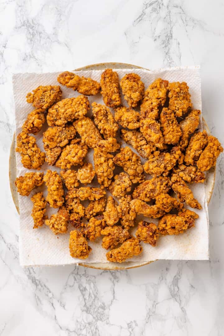 Vegan popcorn chicken features tender soy curls in a crunchy KFC-style breading served with a maple Dijon sauce. It beats takeout any day! Vegan popcorn chicken on a pate lined with paper towels.