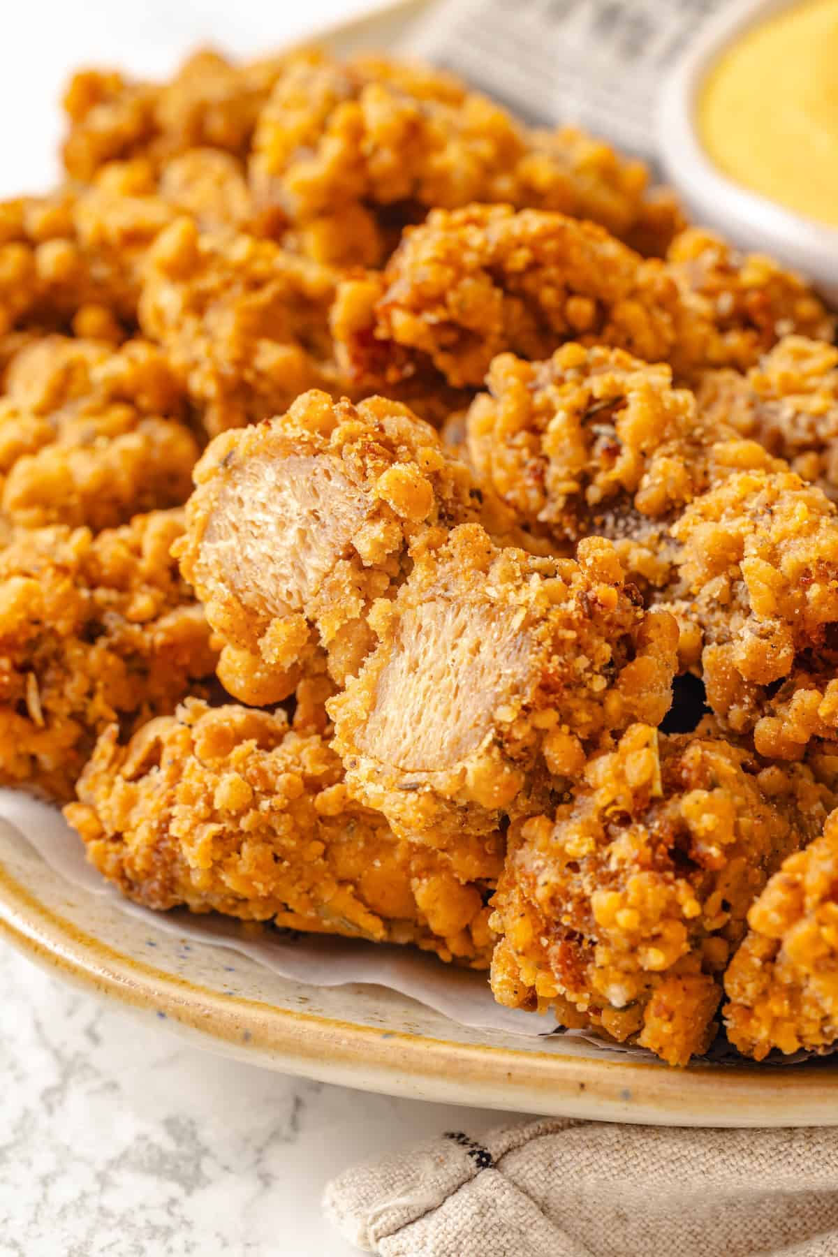 Vegan popcorn chicken features tender soy curls in a crunchy KFC-style breading served with a maple Dijon sauce. It beats takeout any day! Close-up image of vegan popcorn chicken. One piece is torn in half to reveal the inside.