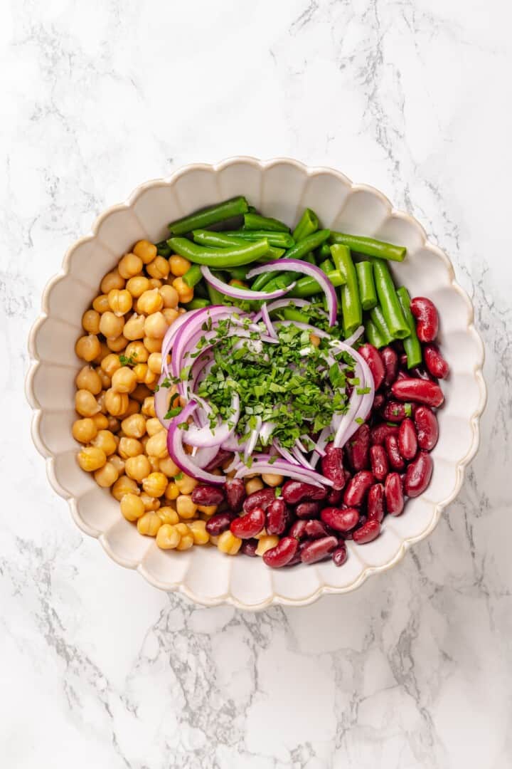 Kidney beans, chickpeas, blanched green beans, slivered red onion, and chopped fresh parsley in a salad bowl. Kidney beans, chickpeas, blanched green beans, slivered red onion, and chopped fresh parsley in a salad bowl.