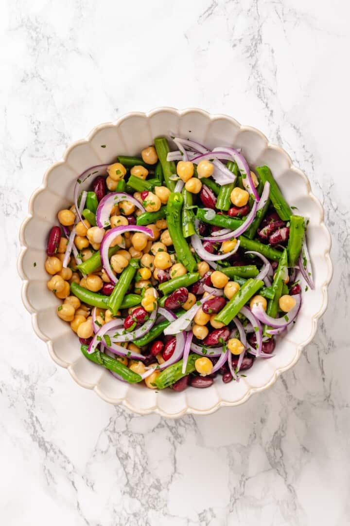 Kidney beans, chickpeas, blanched green beans, slivered red onion, and chopped fresh parsley in a salad bowl. Kidney beans, chickpeas, blanched green beans, slivered red onion, and chopped fresh parsley tossed together in a salad bowl.
