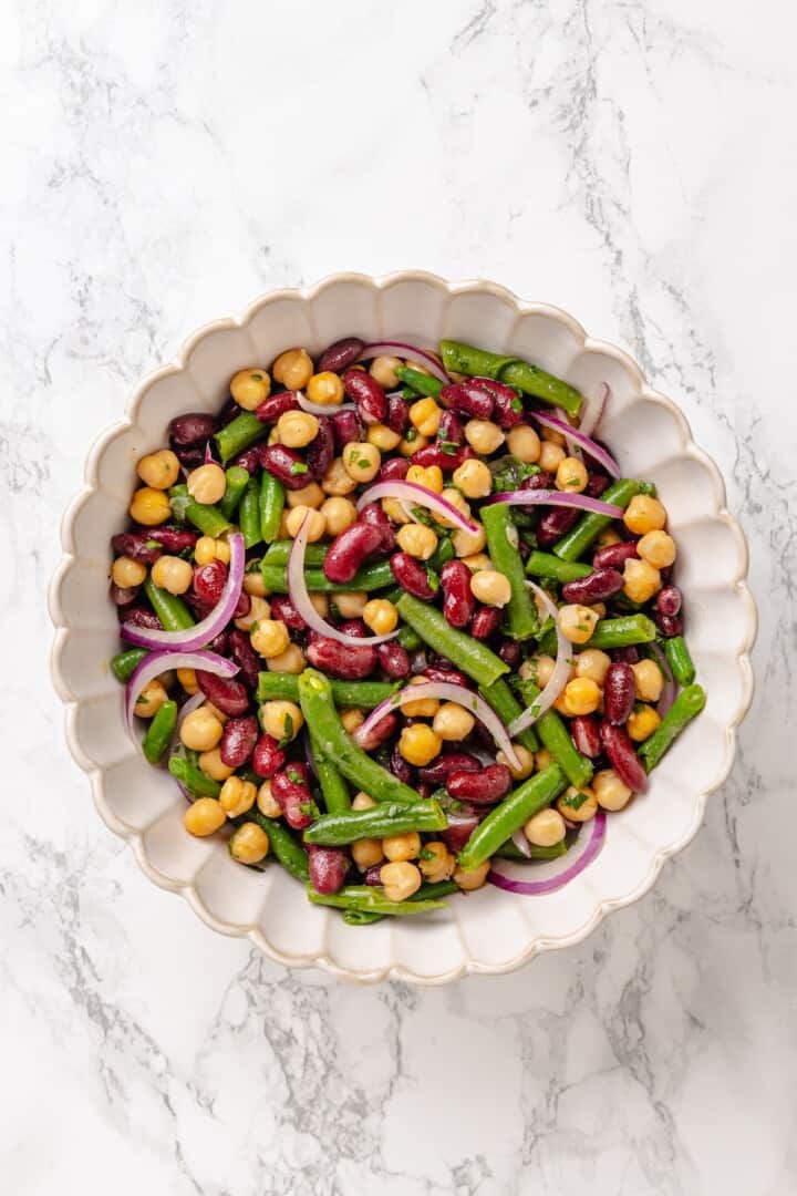 Kidney beans, chickpeas, blanched green beans, slivered red onion, and chopped fresh parsley in a salad bowl. Three bean salad after being chilled in the fridge for 1 hour.