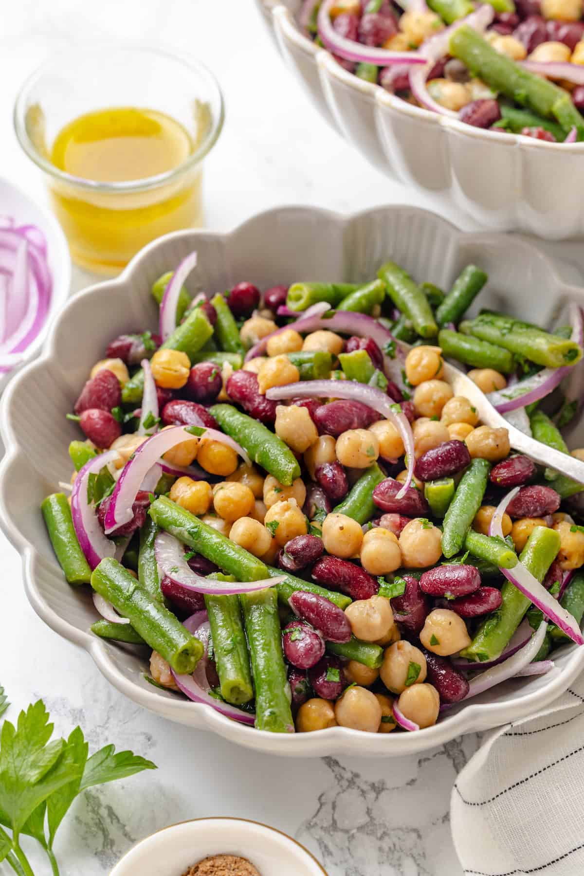 Three bean salad is made with creamy kidney beans, chickpeas, and crisp green beans marinated in a perfectly balanced maple-Dijon dressing. A serving bowl loaded with the best three bean salad.