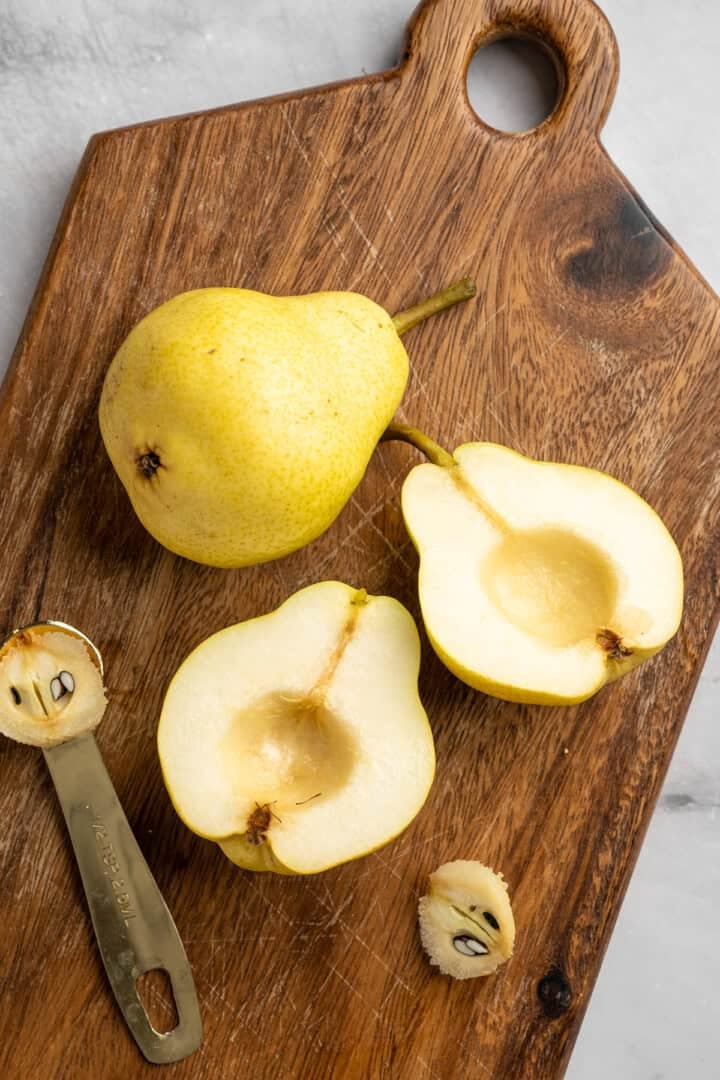 These easy, tender cinnamon baked pears are perfectly caramelized in a glossy sauce of maple syrup, cinnamon, and their own sweet juices. Cored pears on a cutting board.