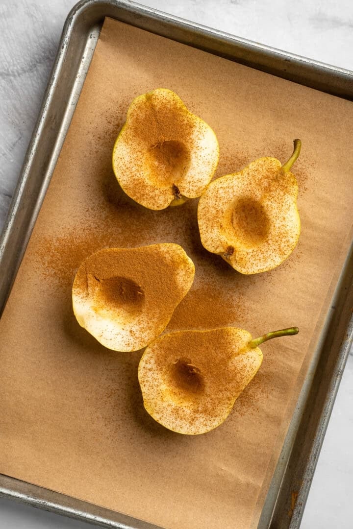 These easy, tender cinnamon baked pears are perfectly caramelized in a glossy sauce of maple syrup, cinnamon, and their own sweet juices. 4 pear halves sprinkled with cinnamon and arranged, cut-side-up, on a baking sheet.