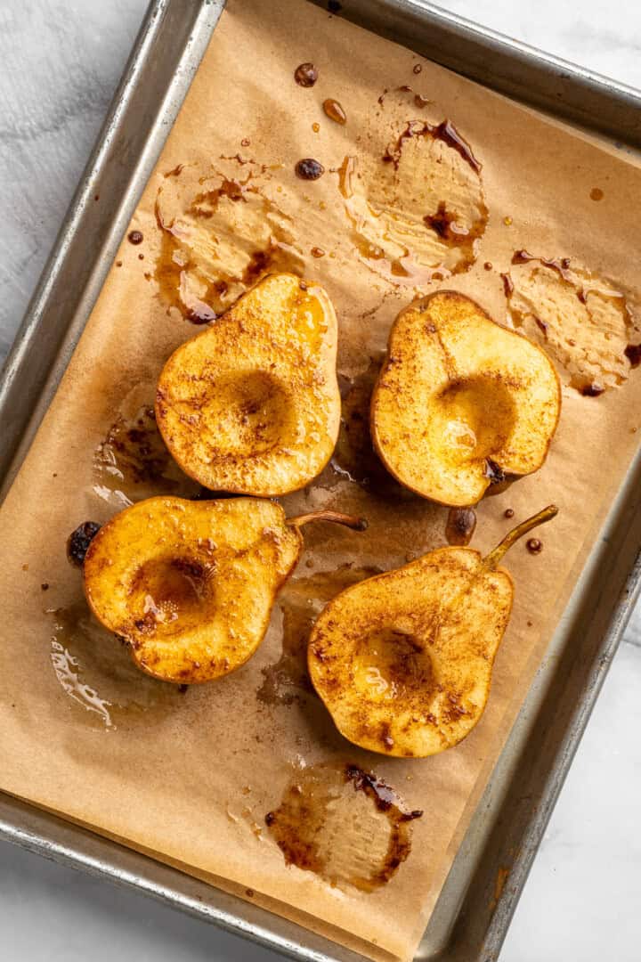 These easy, tender cinnamon baked pears are perfectly caramelized in a glossy sauce of maple syrup, cinnamon, and their own sweet juices. Baked cinnamon pears on a sheet pan.