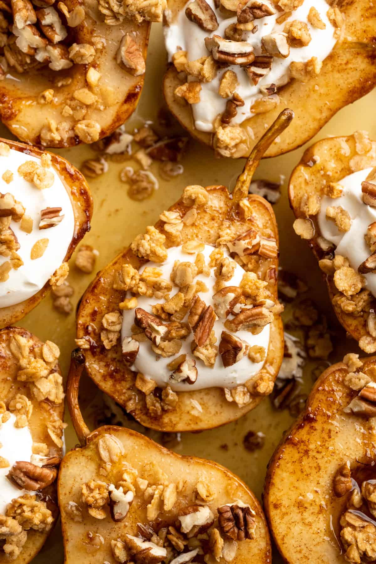 These easy, tender cinnamon baked pears are perfectly caramelized in a glossy sauce of maple syrup, cinnamon, and their own sweet juices. Overhead image of baked pears topped with coconut cream and pumpkin granola.