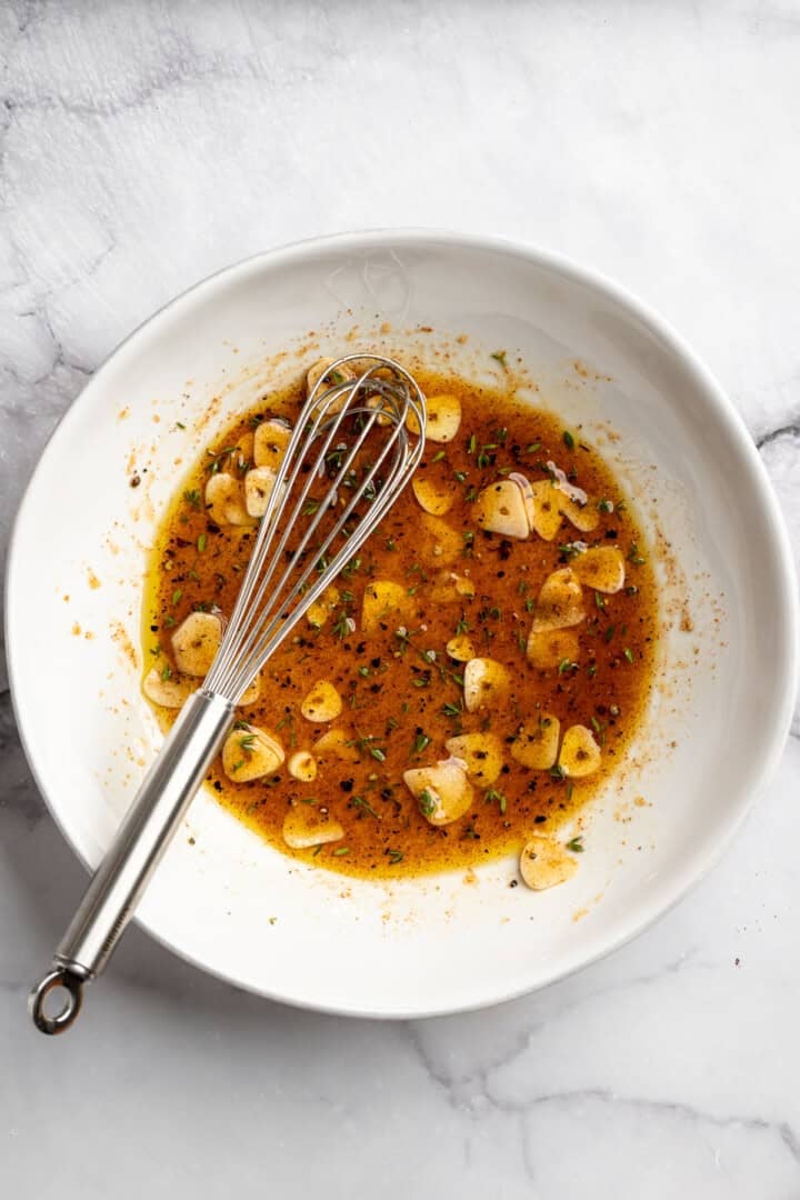 These perfectly caramelized maple roasted carrots are served with a vibrant chimichurri made from the carrot greens themselves. Garlic, coconut oil, maple syrup, thyme, and seasonings mixed together in a bowl.