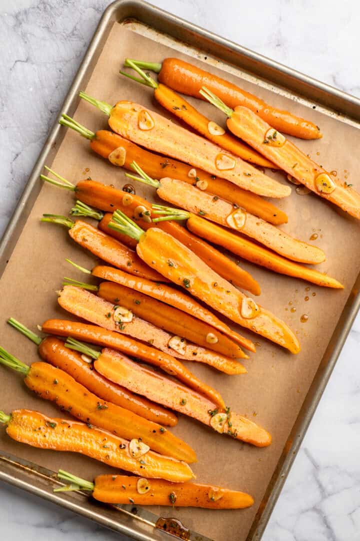 These perfectly caramelized maple roasted carrots are served with a vibrant chimichurri made from the carrot greens themselves. Seasoned carrots spread over a baking sheet ready to go in the oven.