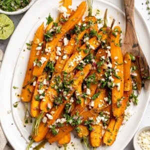 Overhead image of a plate of maple roasted carrots topped with vegan feta and carrot top chimichurri.