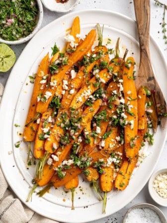 Overhead image of a plate of maple roasted carrots topped with vegan feta and carrot top chimichurri.