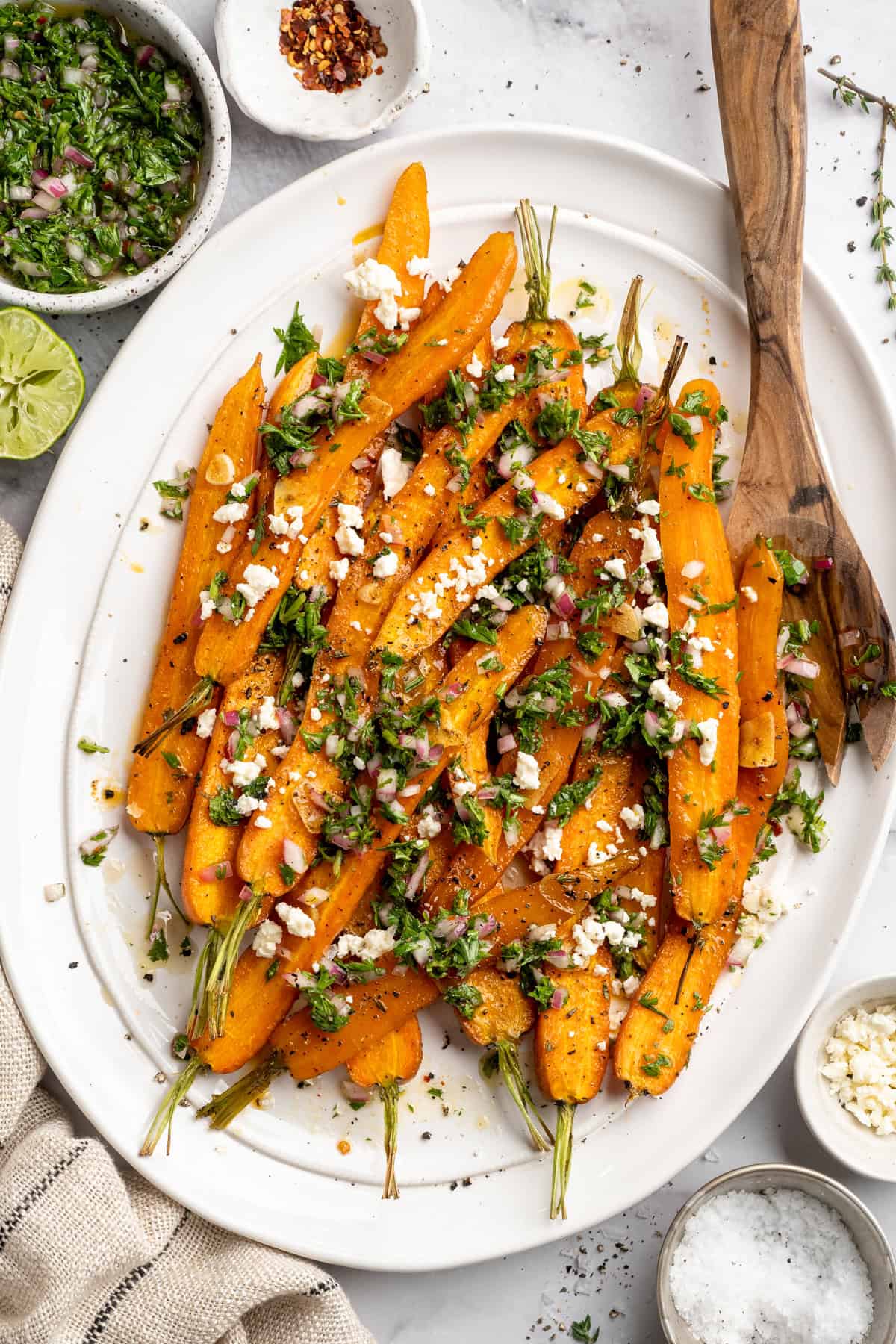 These perfectly caramelized maple roasted carrots are served with a vibrant chimichurri made from the carrot greens themselves. Overhead image of a plate of maple roasted carrots topped with vegan feta and carrot top chimichurri.