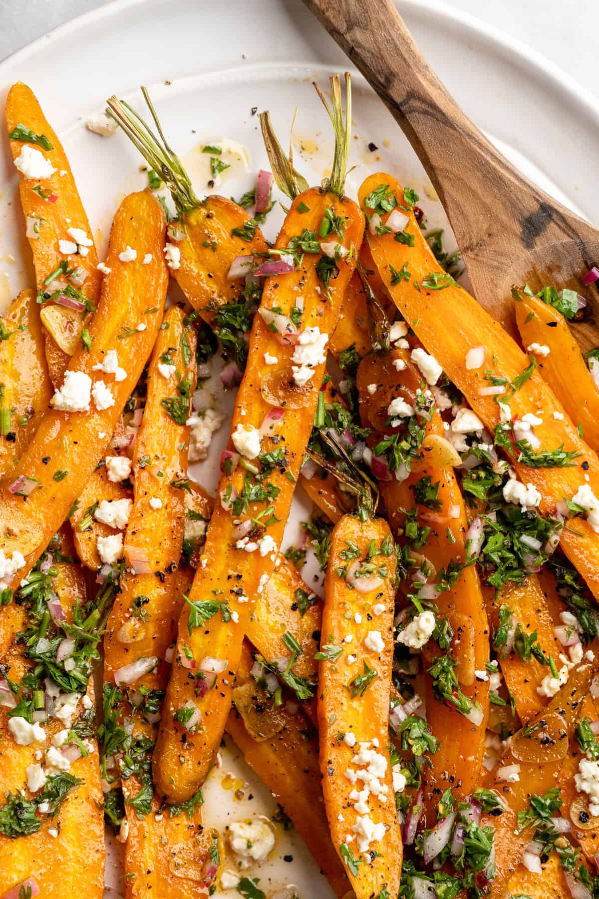 These perfectly caramelized maple roasted carrots are served with a vibrant chimichurri made from the carrot greens themselves. A plate of maple roasted carrots topped with vegan feta and carrot greens chimichurri.